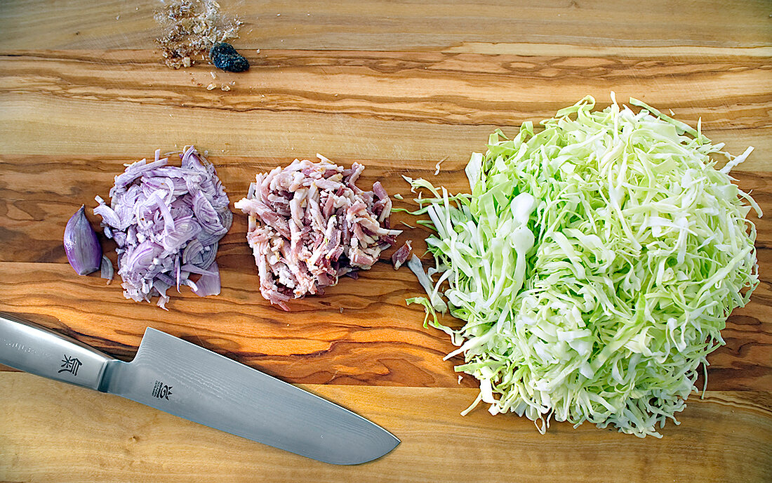 Chopped shallots, bacon and cabbage with knife on cutting board