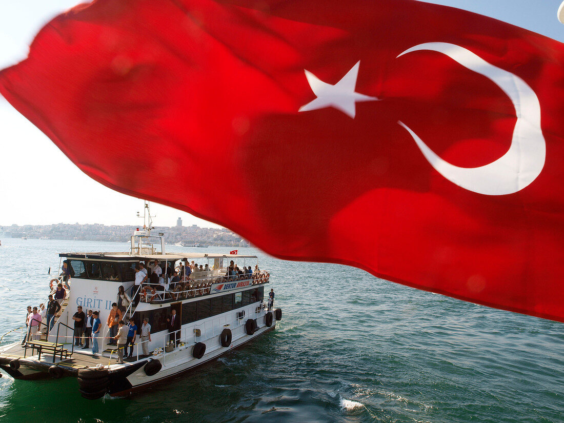 View of Turkish flag and people in transport ferry across Bosphorus, Istanbul, Turkey