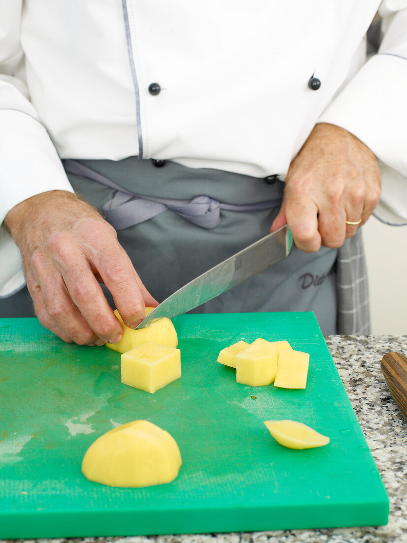 Potatoes being chopped potatoes with knife on cutting board