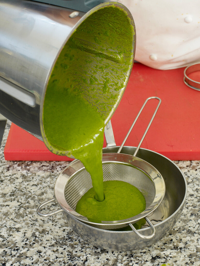 Green puree being strained through strainer in pan