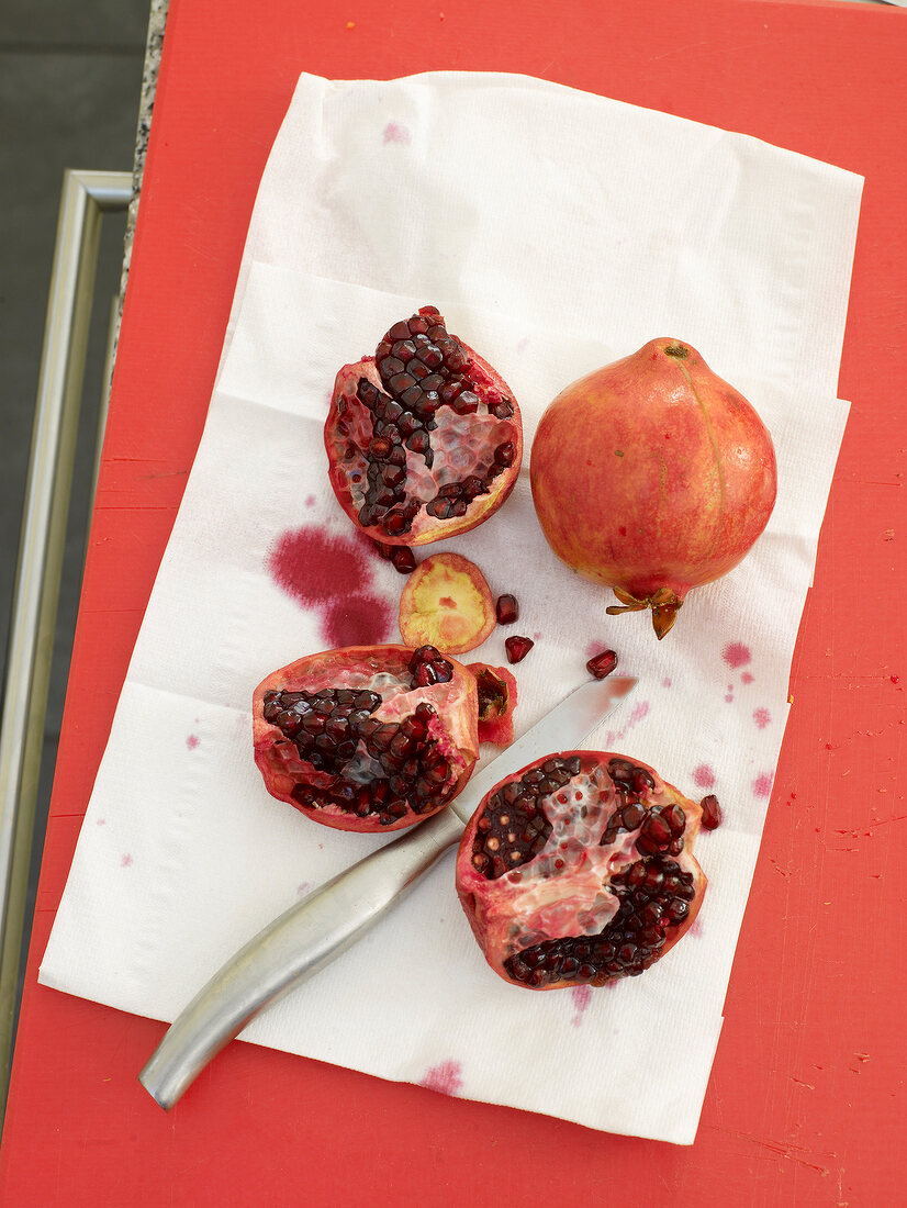 Halved pomegranate on board with tissue and knife