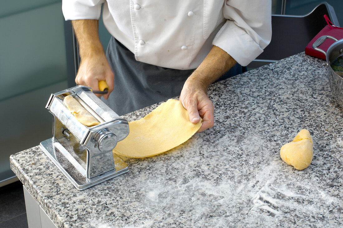 Close-up of man's hand preparing pasta sheet on machine