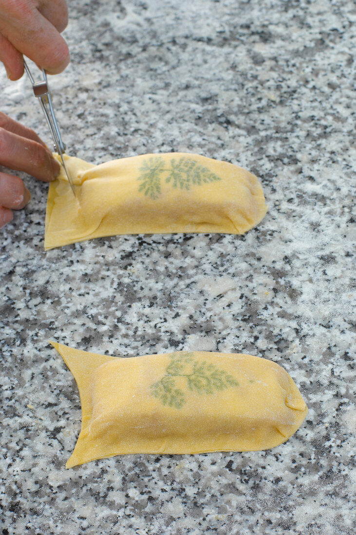 Close-up of man's hand shaping pasta dough with chervil leaf and salmon fillet