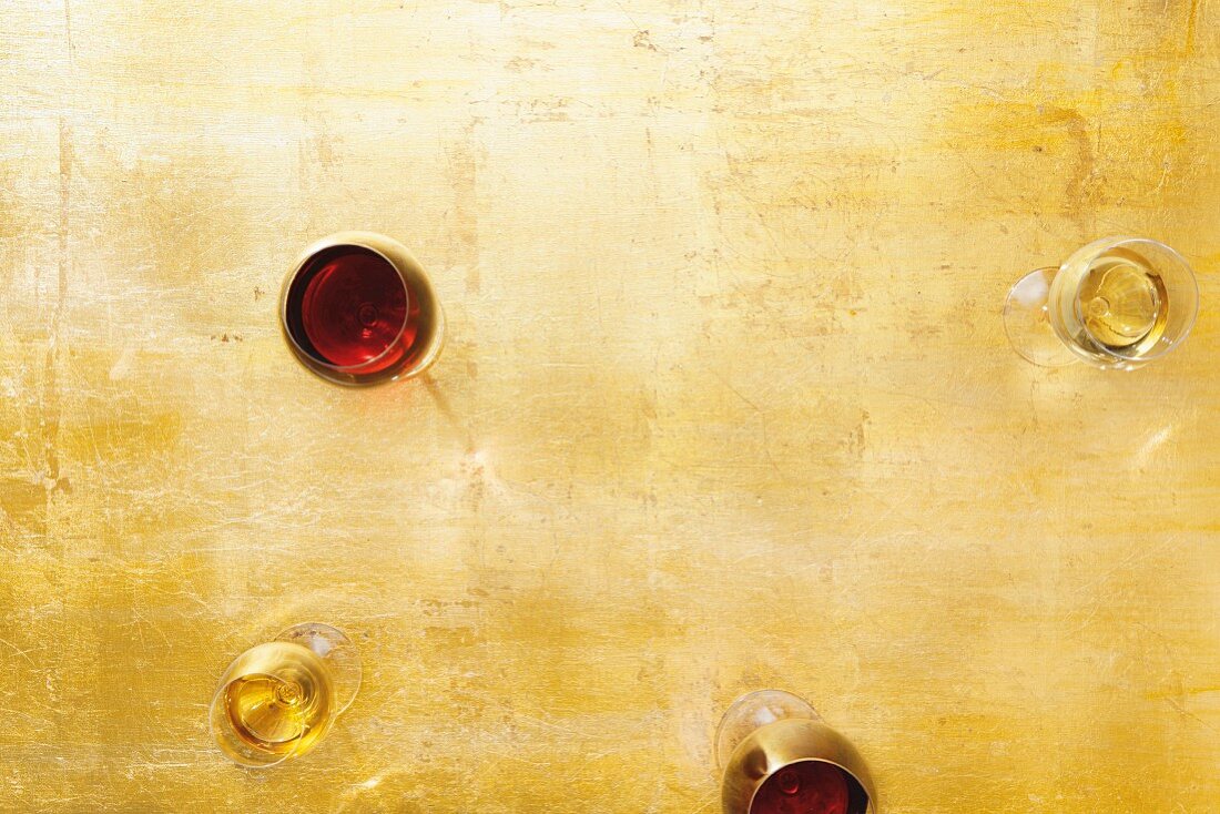 Glasses of white wine and red wine on a golden surface (seen from above)