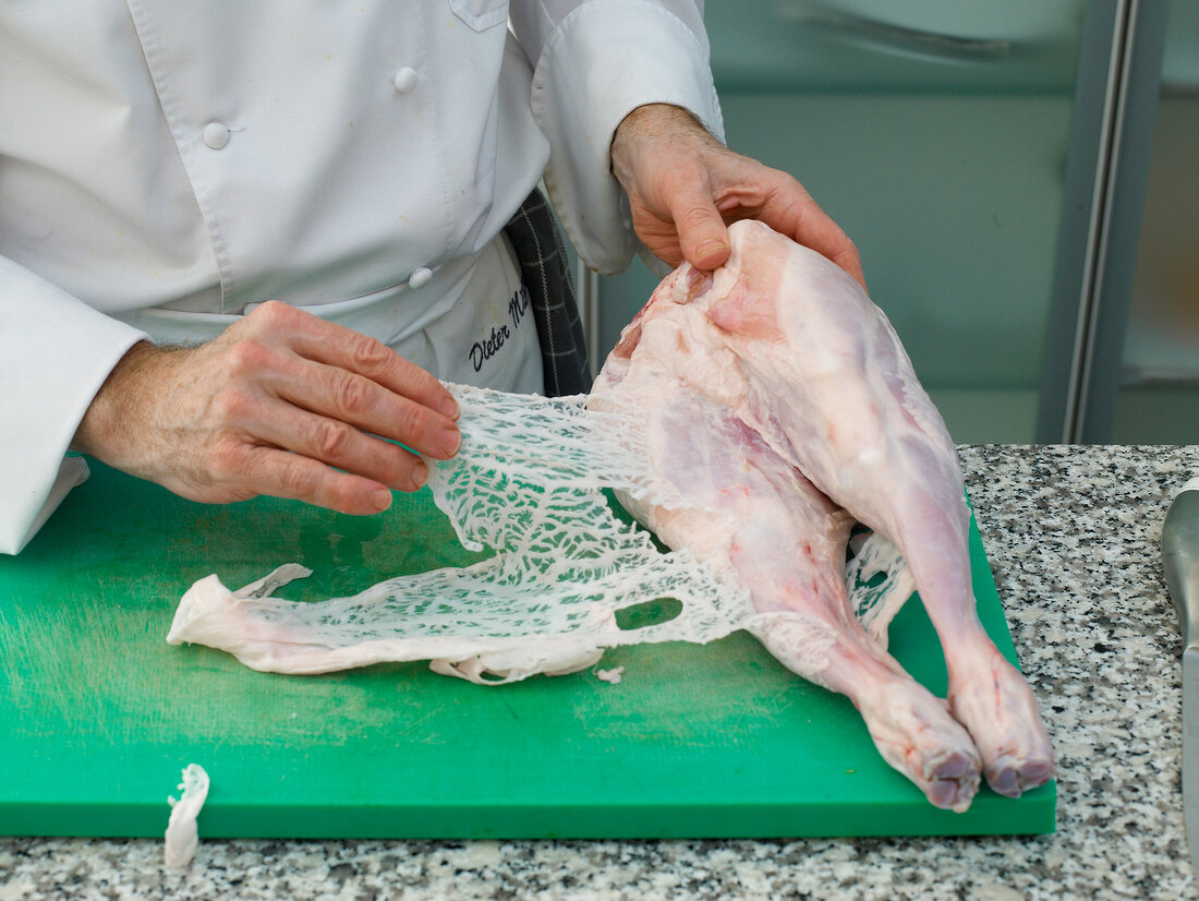 Chef peeling of the skin from lamb's leg