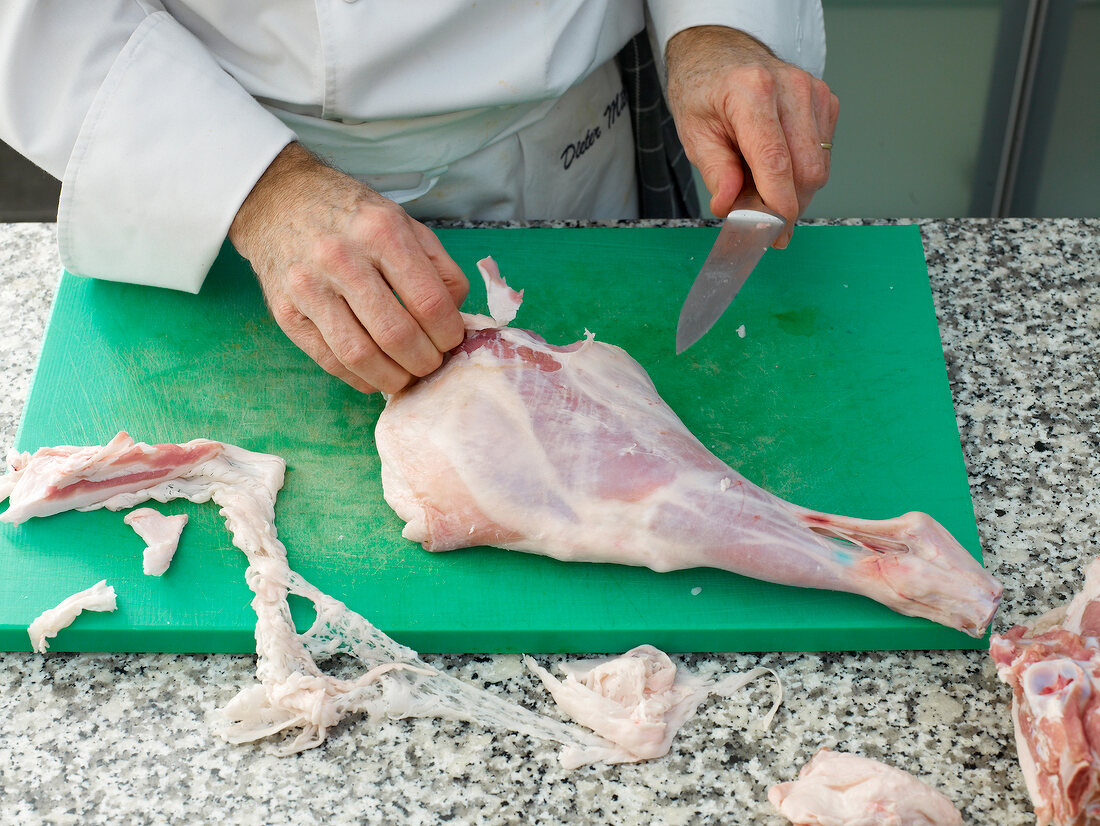 Chef peeling of the skin from lamb's leg