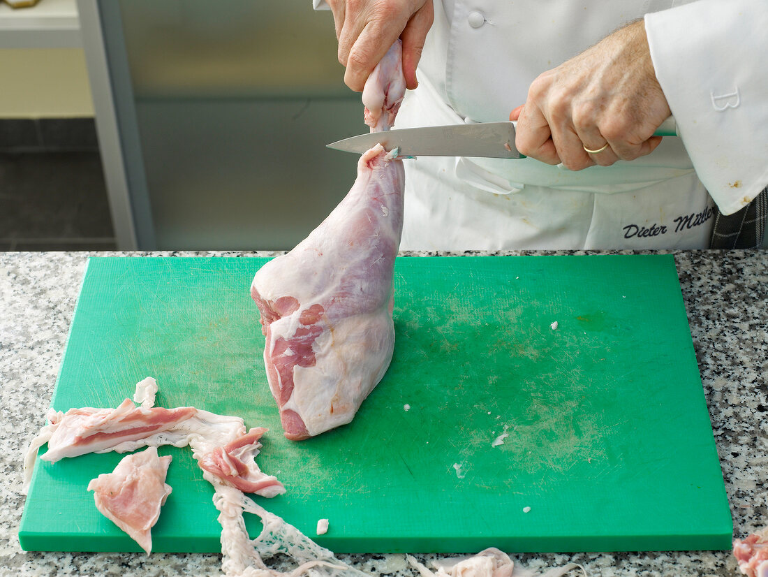 Chef cutting lamb's leg with knife