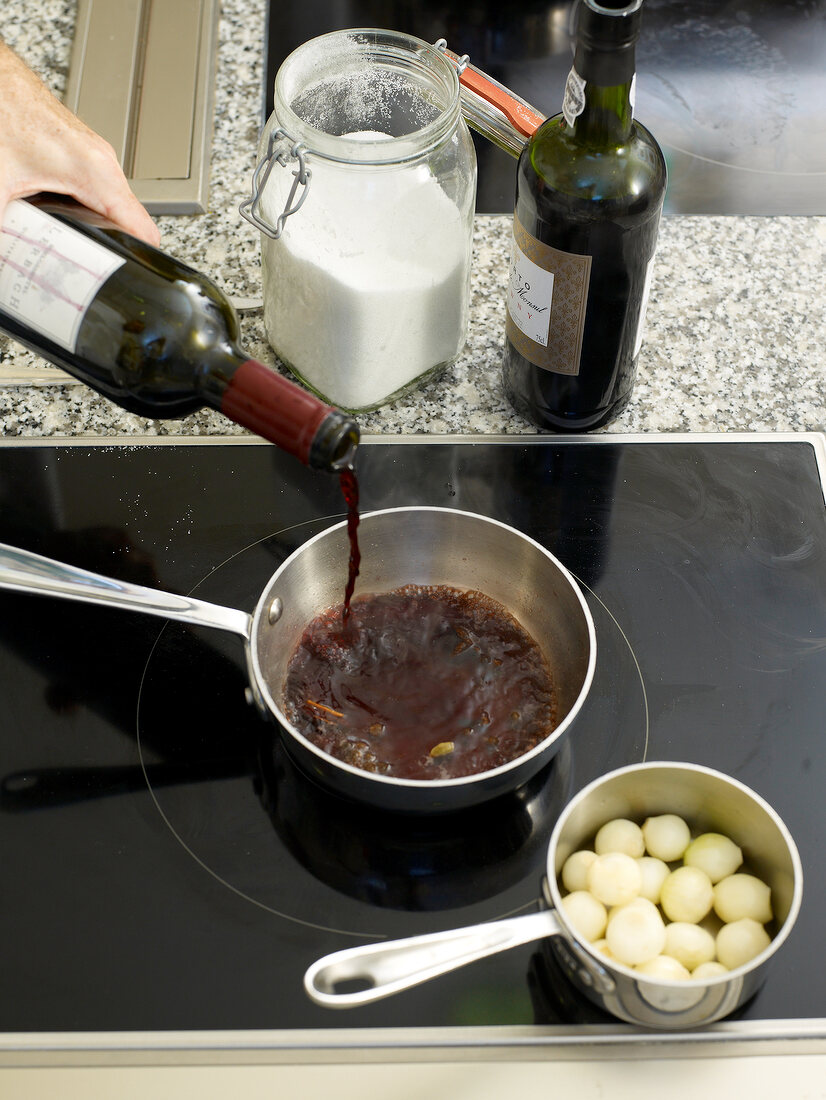 Red wine being added to ingredients for pickled pearl onions in pan