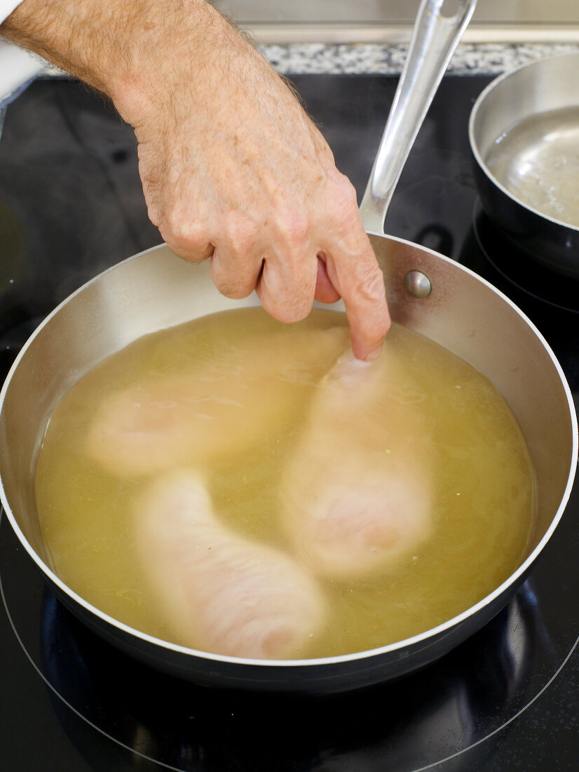 Corn-fed chicken breast pieces dipped in oil in saucepan