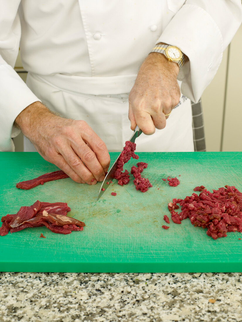 Cutting beef in pieces with knife on cutting board