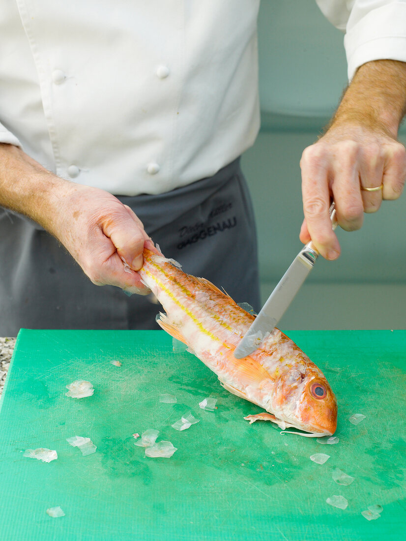 Removing skin of red mullet by knife on chopping board