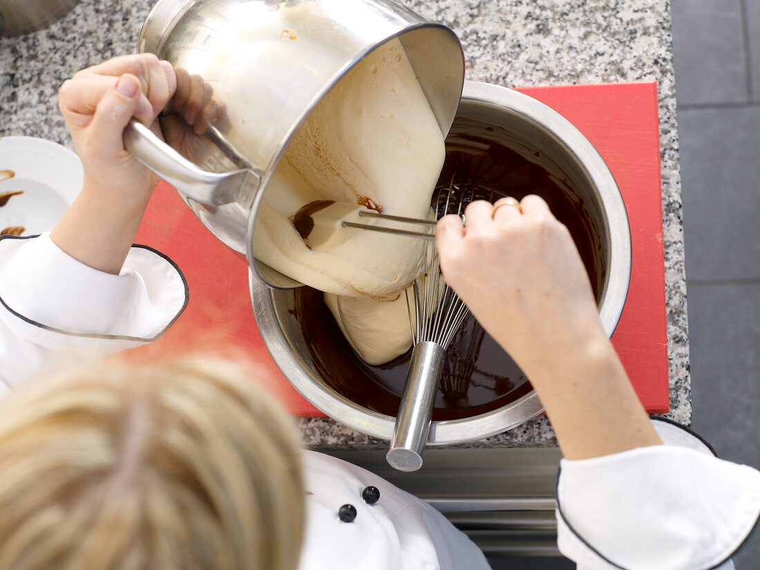 Adding cream to chocolate mixture in bowl with whisk