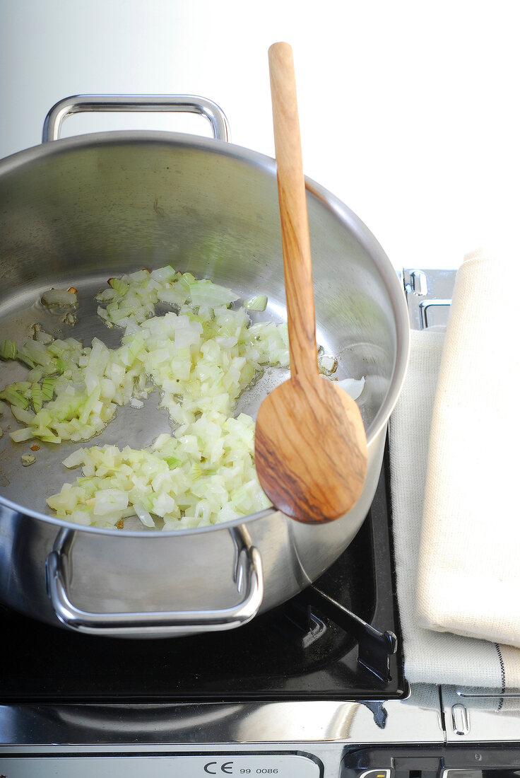 Frying onions in casserole with wooden spoon for preparation of tomato sauce, step 1