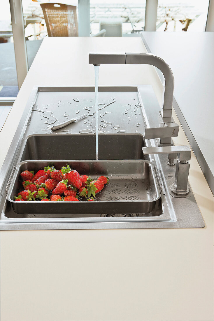 Fresh strawberries in sieve being washed in sink