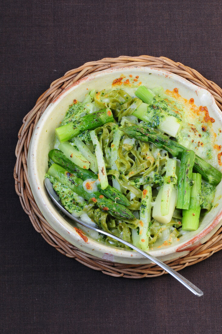 Overhead view of green lasagne in bowl on wicker coaster