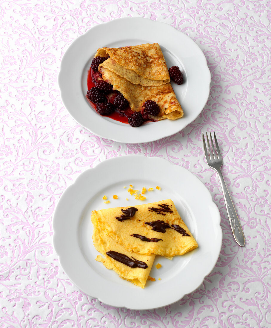 Two plates of nut pancakes with blackberries and vienna cream crepes
