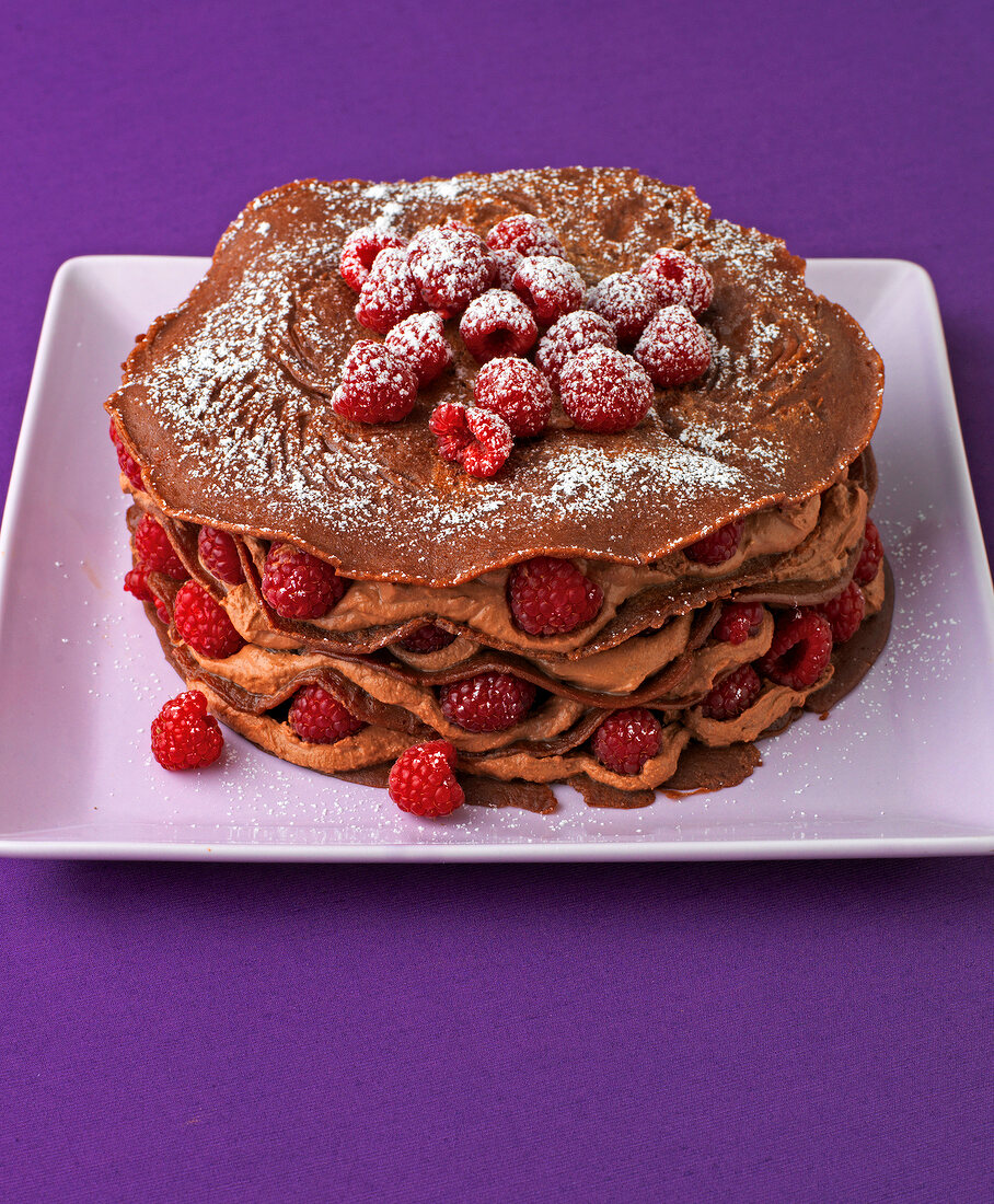 Mocha chocolate crepes cake with raspberries and icing sugar on plate
