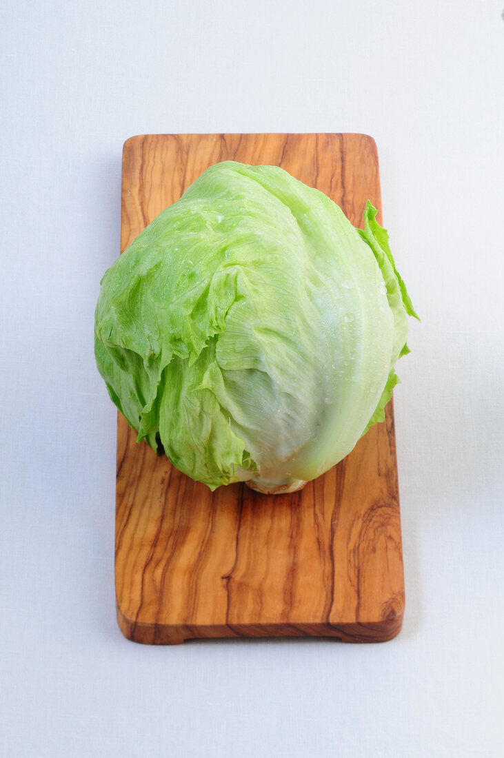 Salate, ein Kopf Eissalat auf einem Holzbrett
