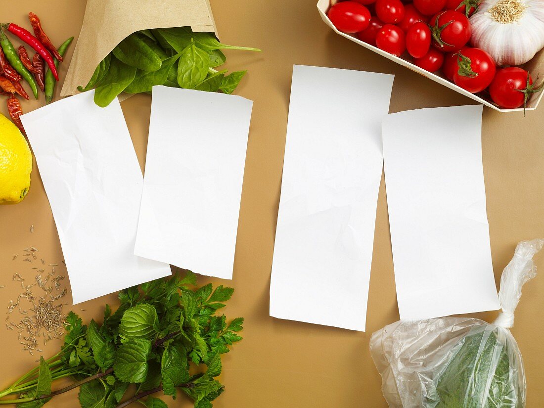 Four blank pieces of paper surrounded by vegetables and herbs