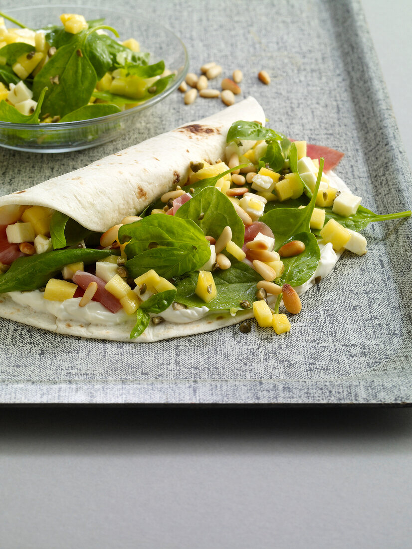 Close-up of wraps with spinach, mango and ham on tray
