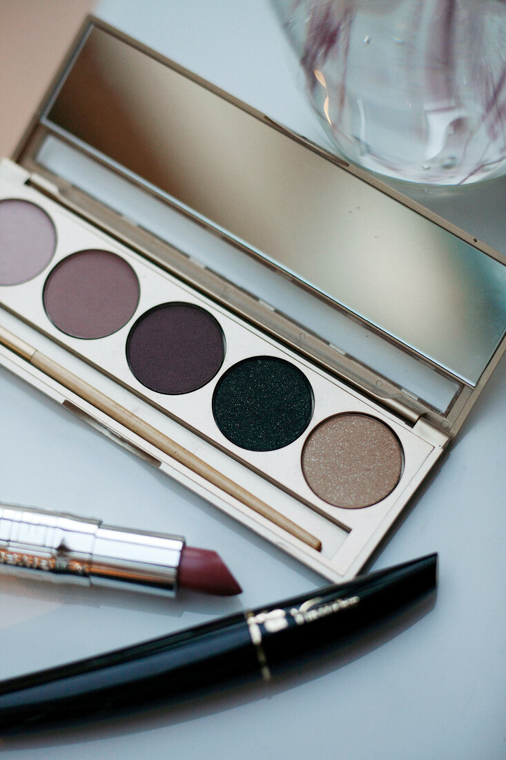 Close-up of lipstick, mascara and various eye shadows in a palette on white background