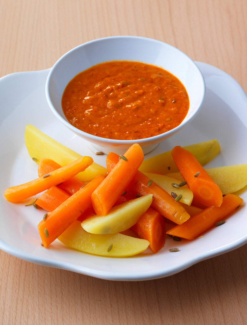 Bowl of garlic cream, sliced carrots and potatoes on plate