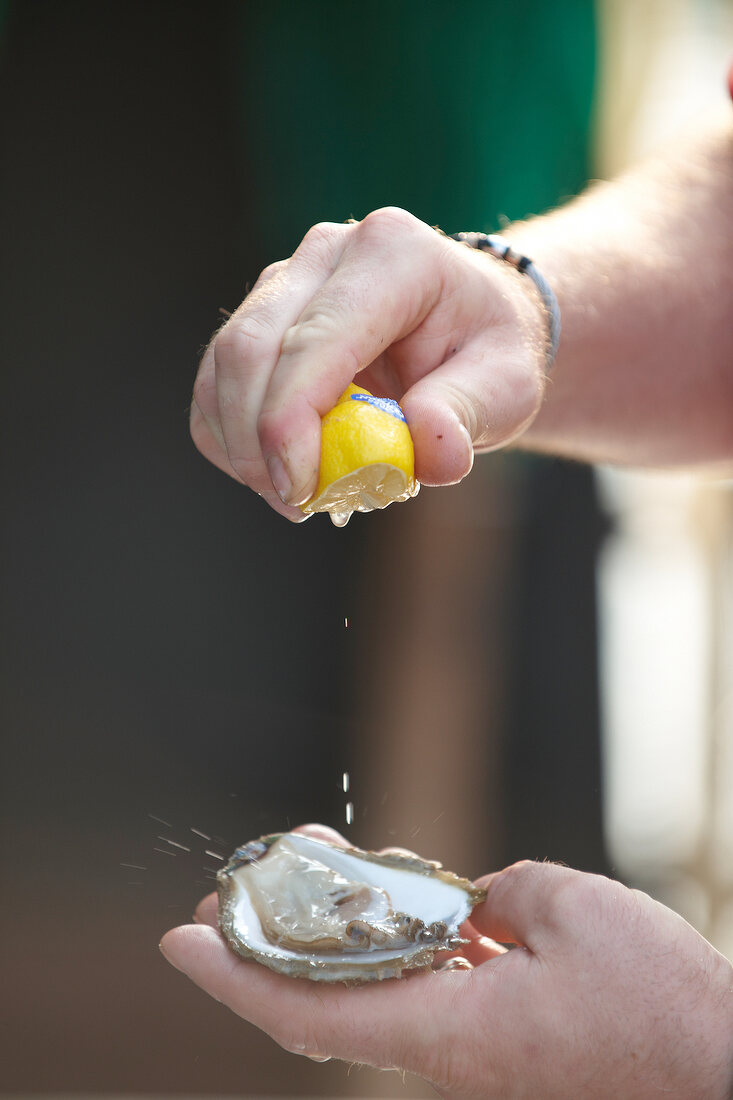 Auster auf Handfläche, wird mit Zitrone beträufelt