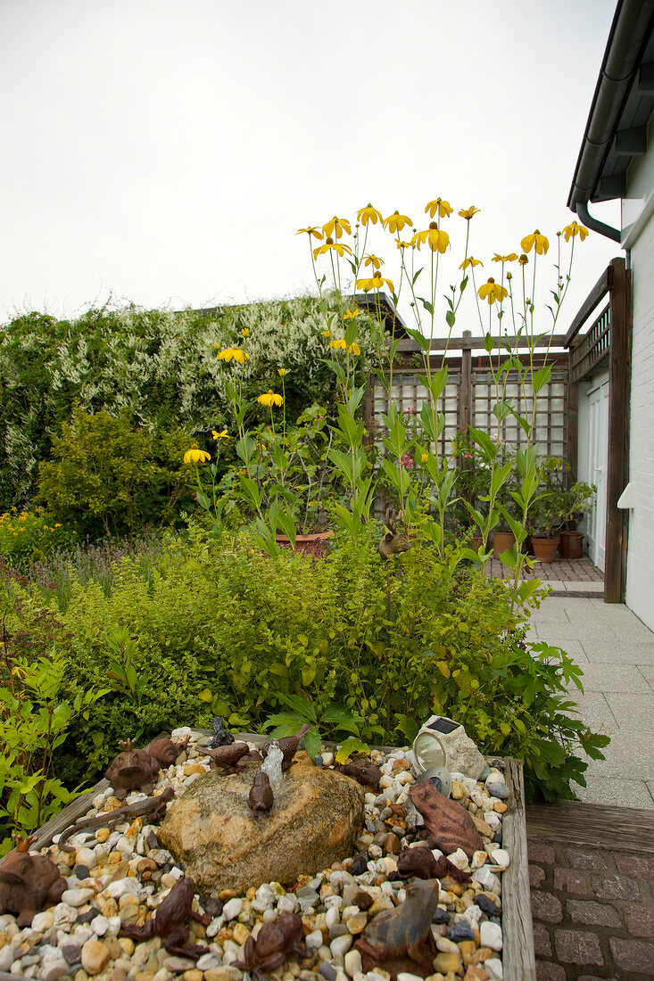 Brunnen mit Kiesel und Steinfiguren, von Rudbeckia Staude umrahmt