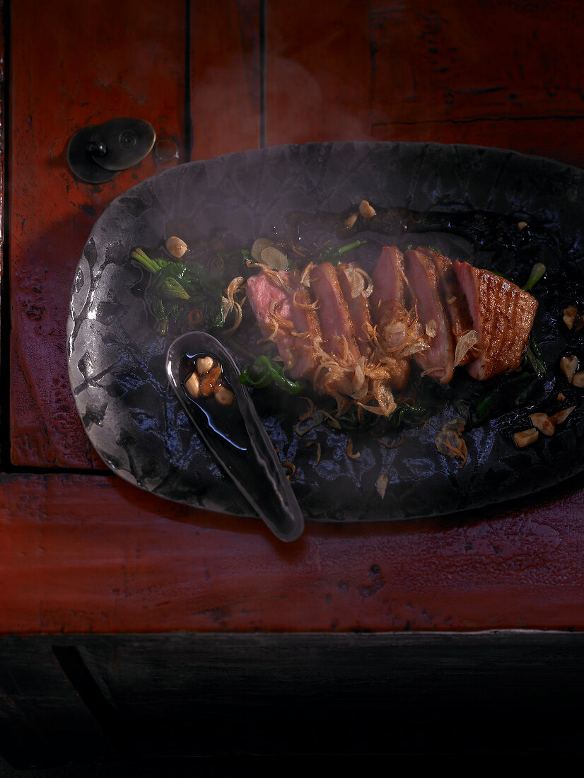 Fried shallots with duck breast, spinach and peanuts on frying pan