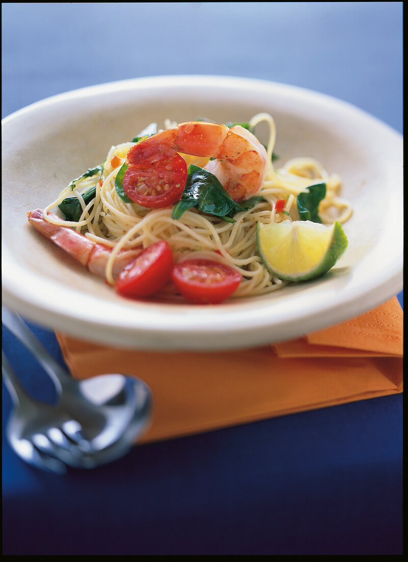Spaghetti pasta garnished with king prawns, cherry tomatoes and lime in serving dish