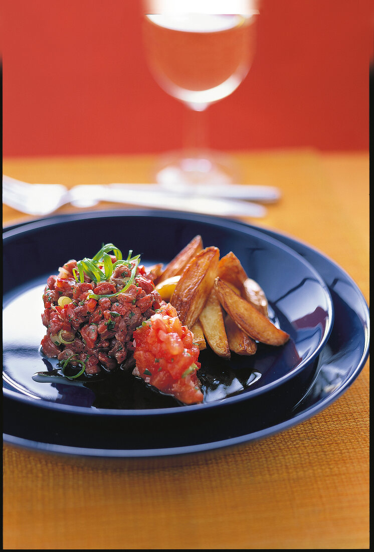 Tartar of ox meat with hot salsa and potato wedges on plate