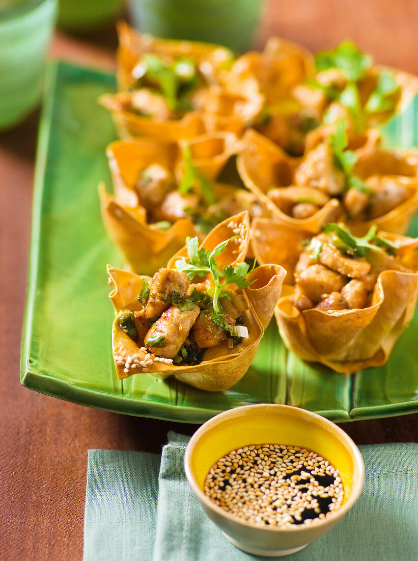 Sesame chicken in pastry shells in serving dish and soy sauce in bowl