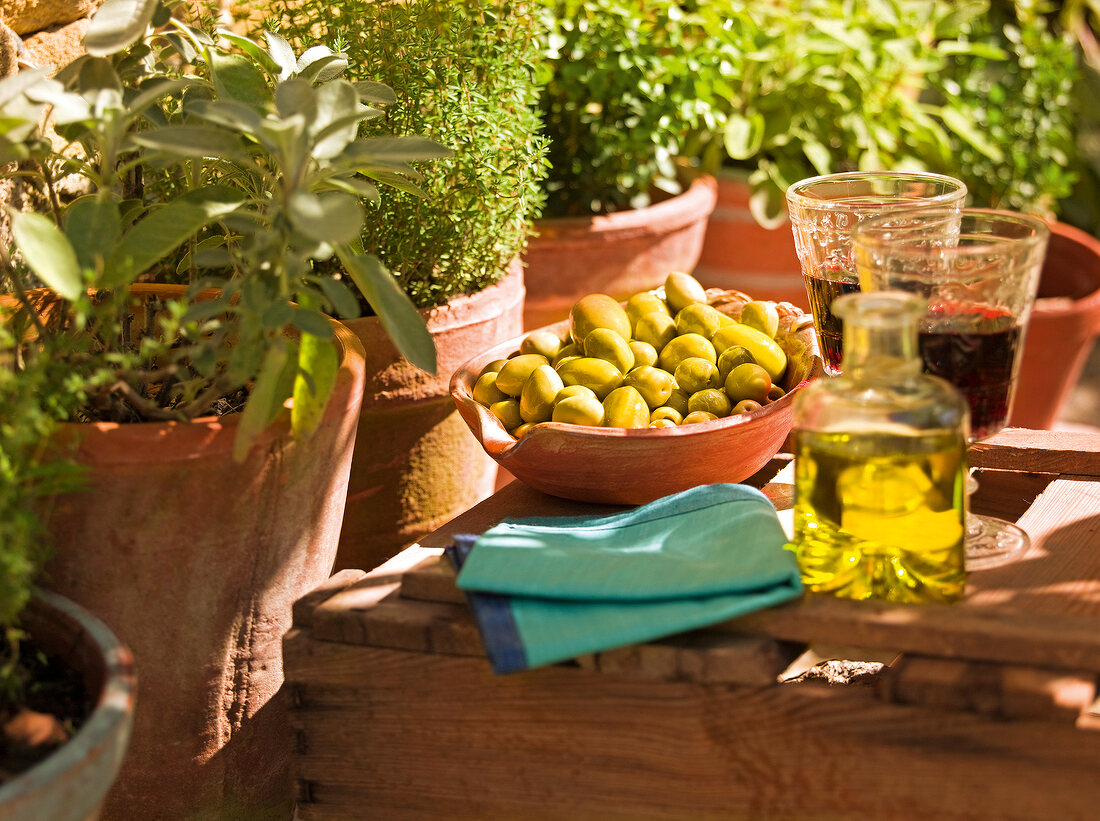 Olives, herbs in terracotta pots on wooden table