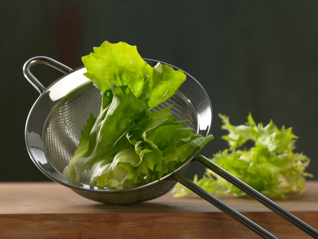 Close-up of salad leaves in colander on wooden surface