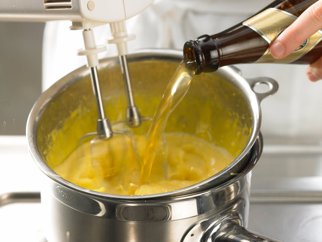 Adding wheat beer and mixing batter in bowl with hand mixer while preparing biersabayon