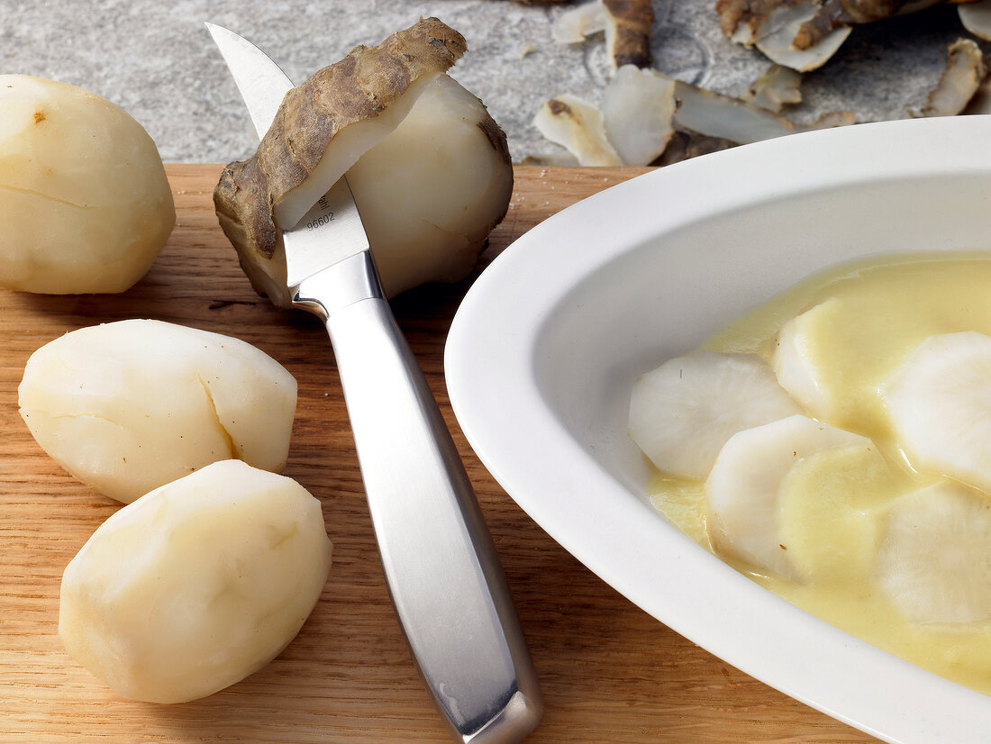 Close-up of Jerusalem artichoke being peeled tubers with knife and marinating in bowl