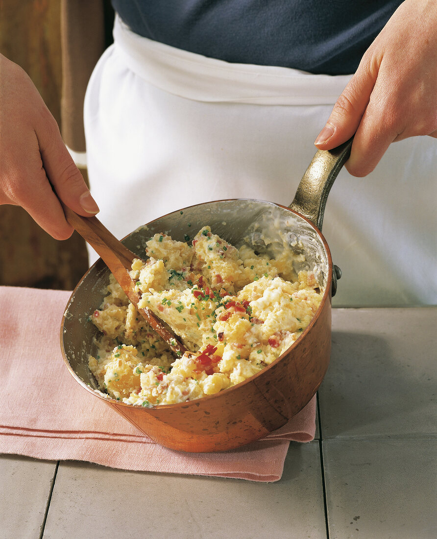 Ramming potatoes with bacon and shallots in saucepan