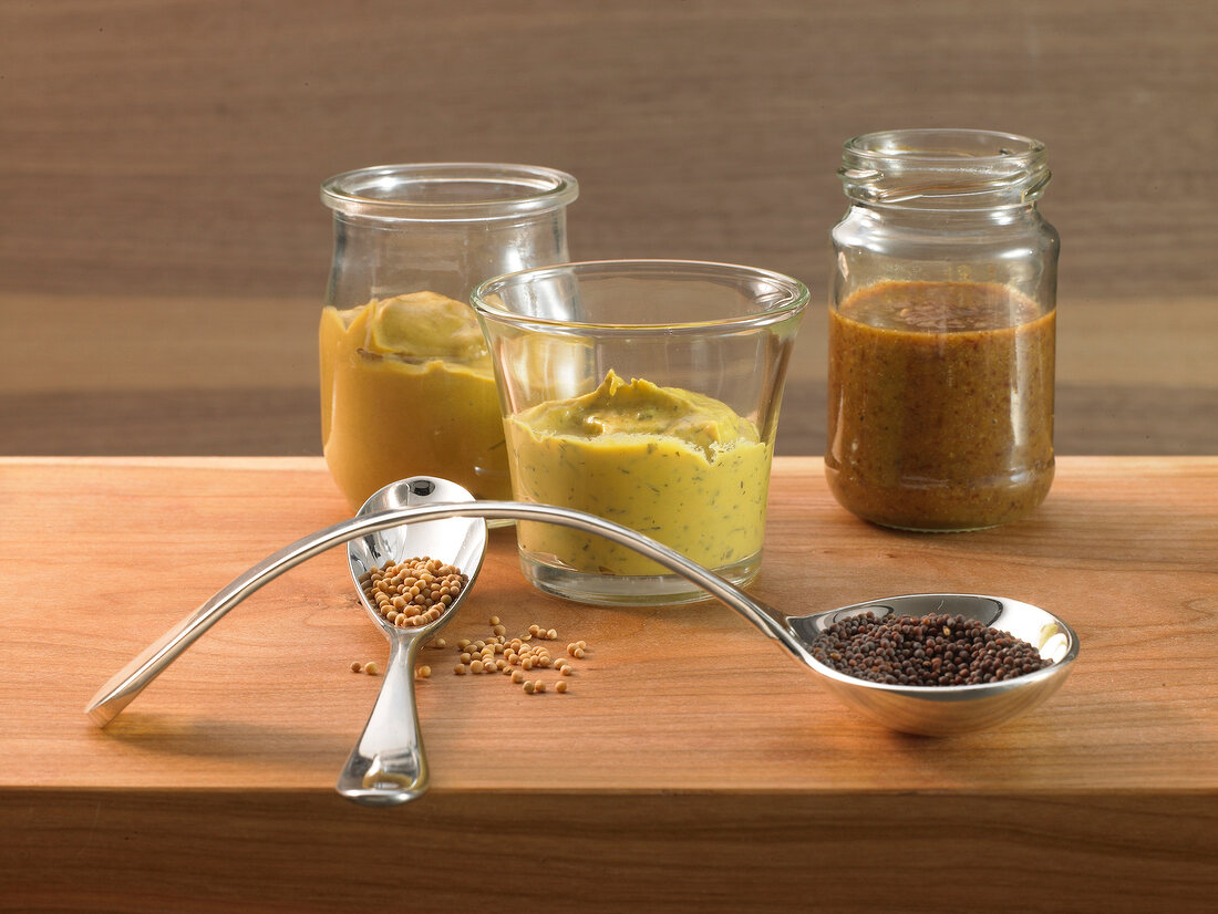 Different types of mustard sauce and mustard seeds on wooden surface