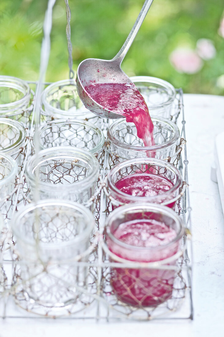 Small glass jars being filled with rose jam