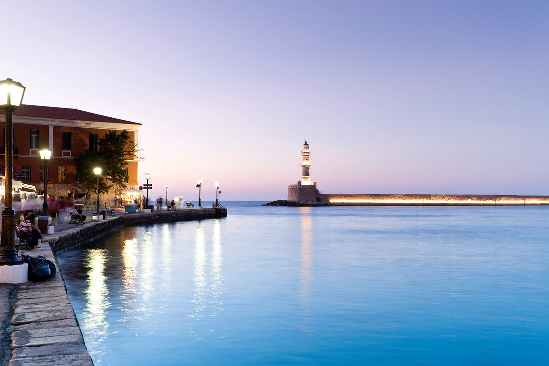 Chania Lighthouse at dawn and people sitting on bench at promenade near sea, Crete, Greek