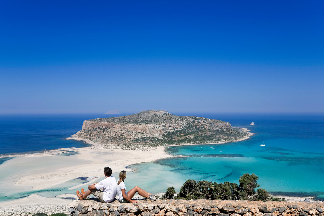 View of couple sitting on beach and looking at Island Gramvoussa, Greece