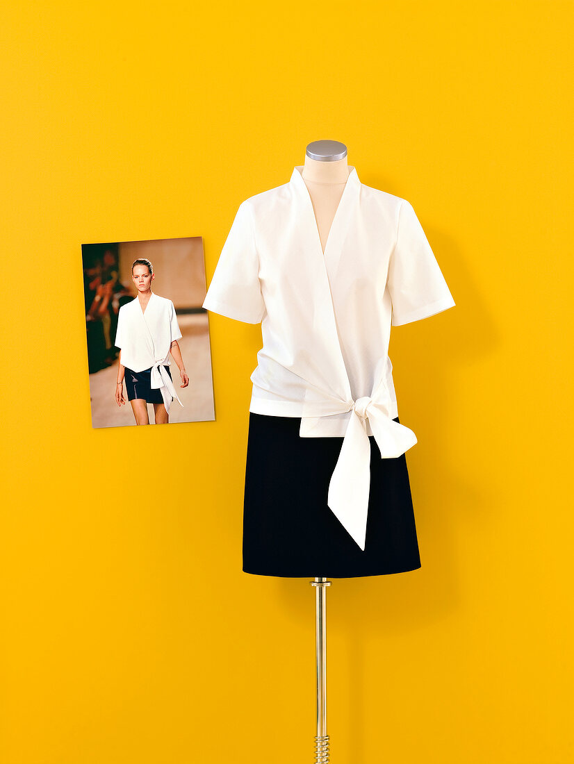 White blouse and black skirt on mannequin against yellow wall