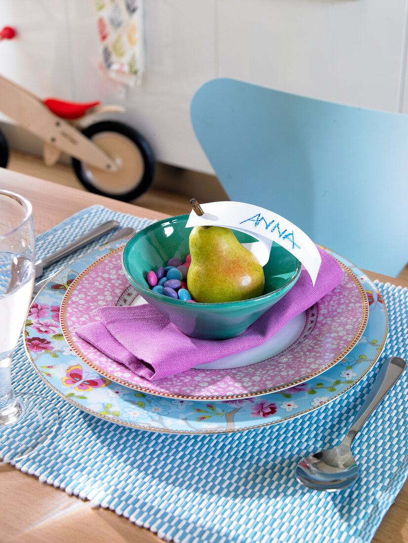 Bowl of confectionery and pear with name card on table