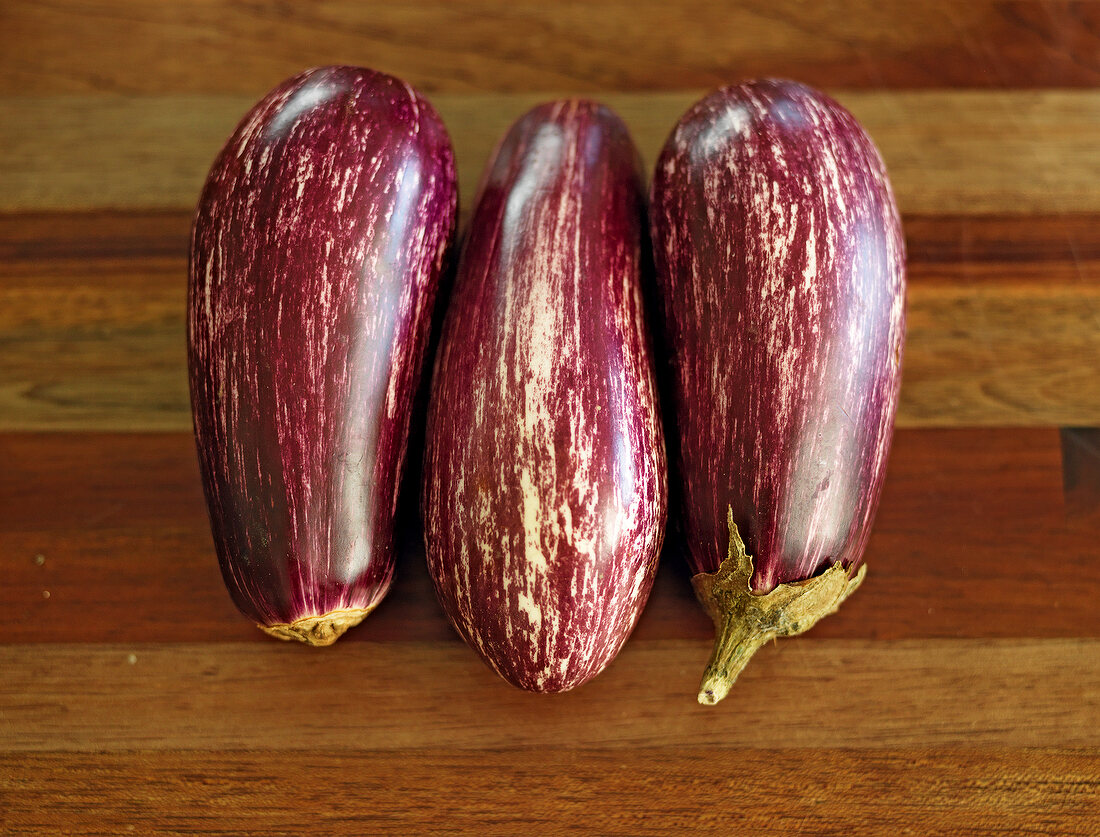 Close-up of three fresh eggplant on wood