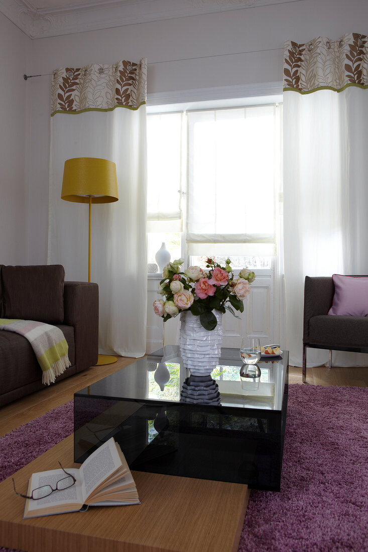 Room with table, flower vase, white patterned curtain and yellow floor lamp