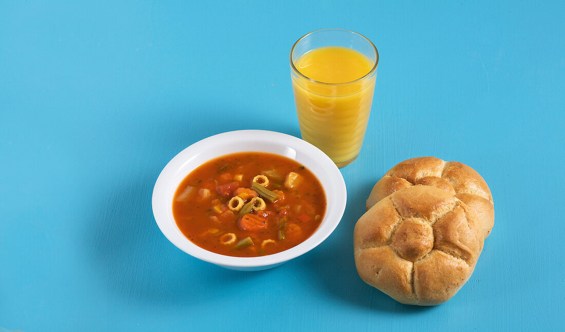 Bowl of vegetable stew, glass of juice and bread on blue background