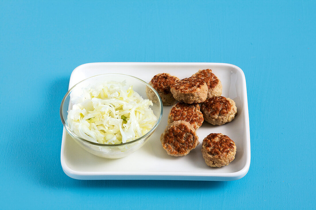 Bowl of coleslaw with mini burgers on white dish