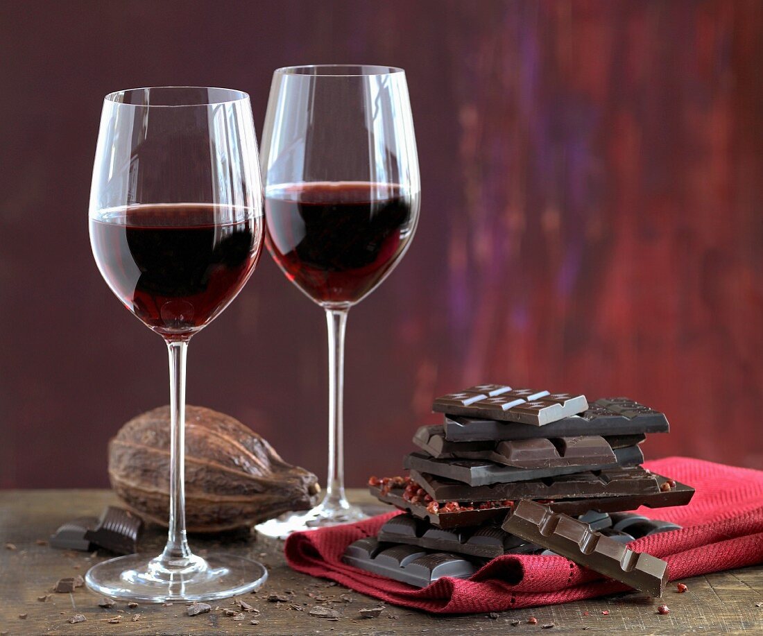 An arrangement of red wine glasses, cocoa beans and a stack of chocolate