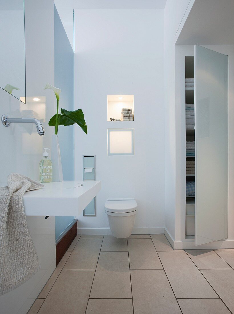 A white bathroom with a wash basin, a suspended toilet and a built in wall cupboard