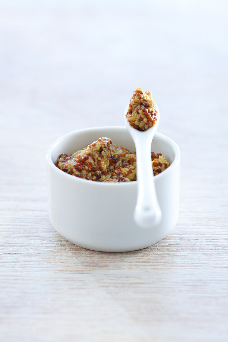 Coarse mustard in small bowl with a spoon